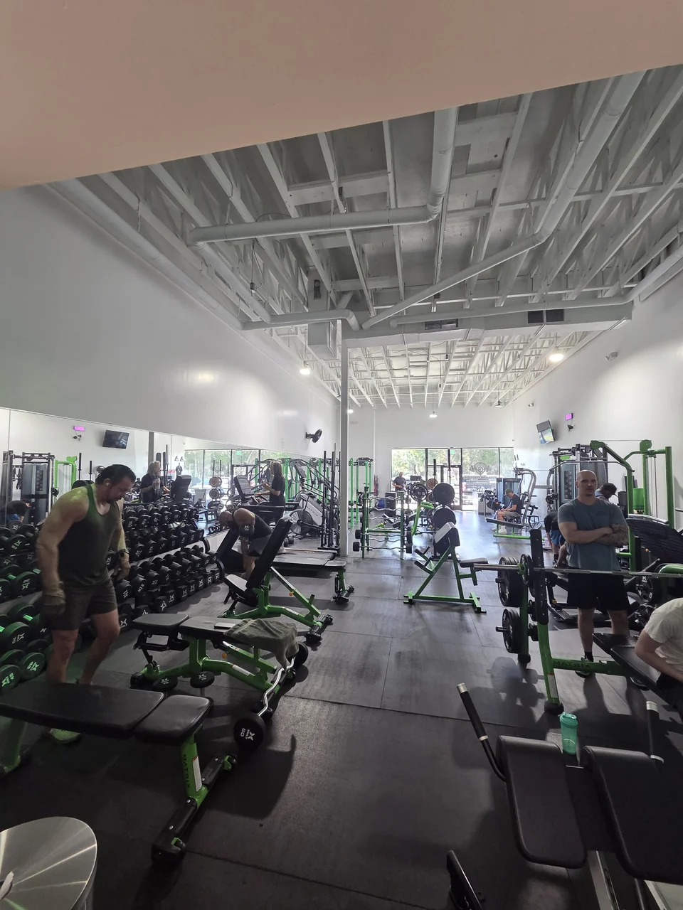 Members training among dumbbells, benches, and green strength equipment at Titan Gym